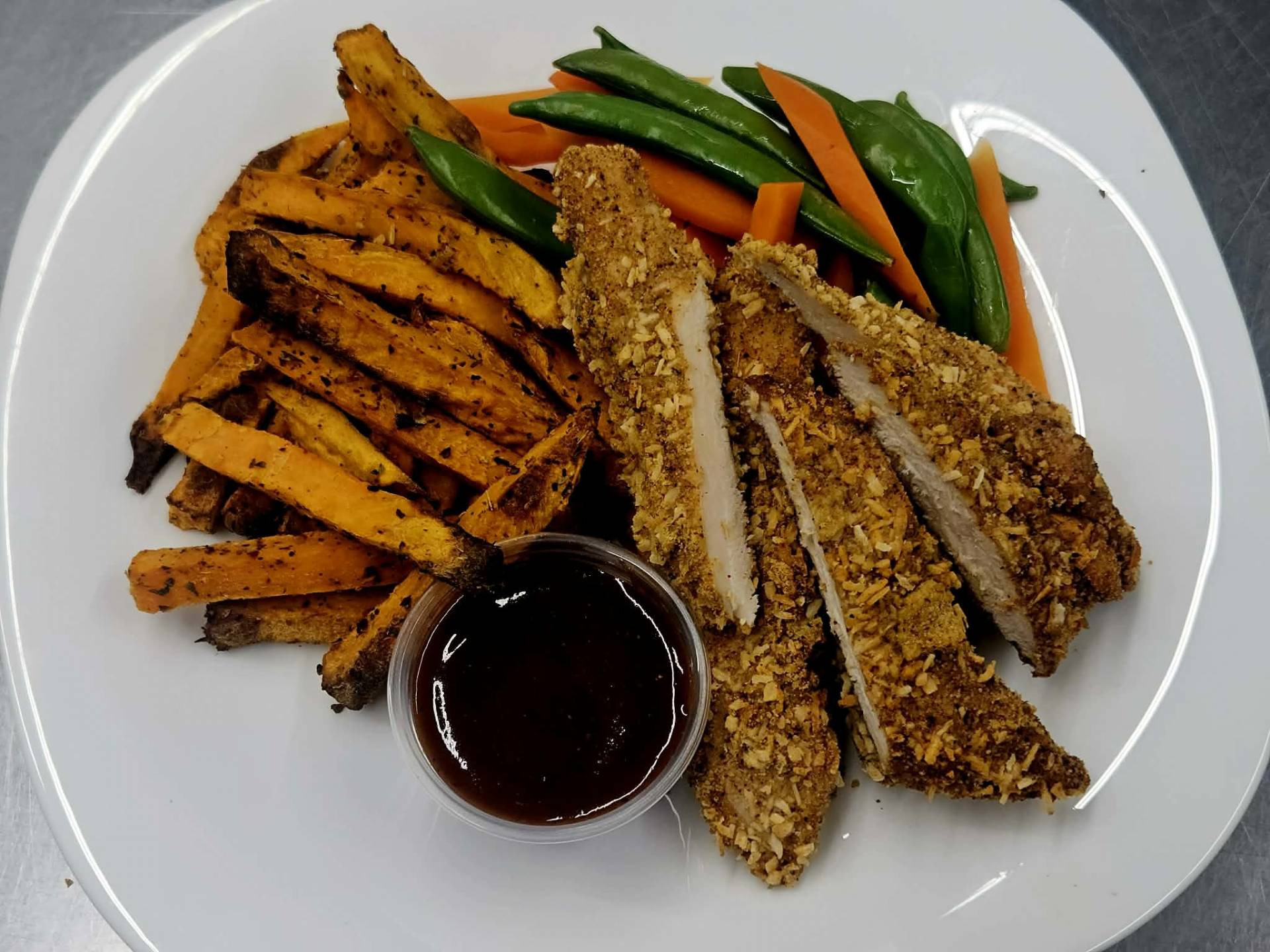 Filets de poulet panés à la noix de coco, frites de patates douces, pois sucrées et carottes